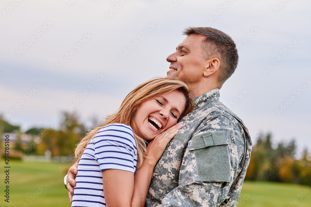 Married soldier hugging wife outdoor. Woman is very happy her husband is back from the army.