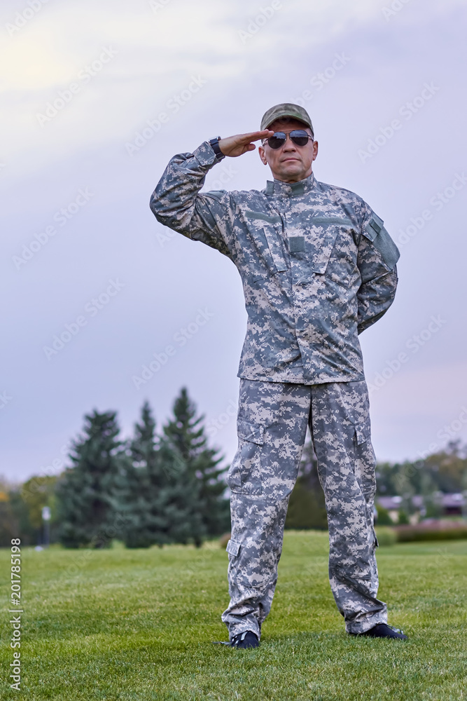 Portrait of full-length soldier saluting. Serious mature sergeant in camouflage uniform outdoors. Portrait of full-length soldier saluting. Serious mature sergeant in camouflage uniform outdoors.