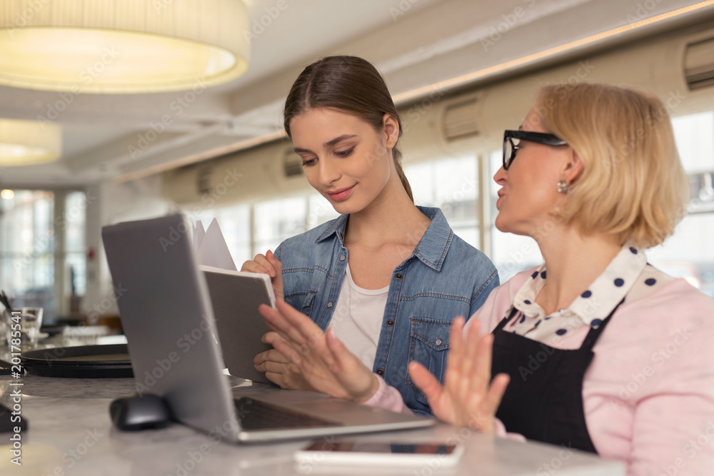 Young employer. Happy young employer holding a notebook and talking with her employee Young employer. Happy young employer holding a notebook and talking with her employee
