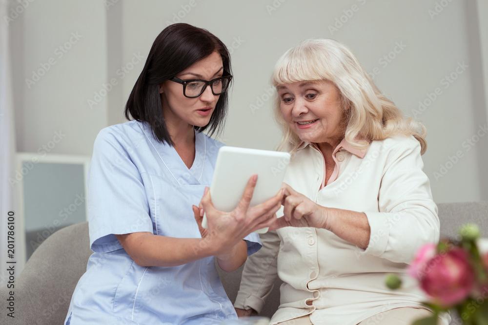 New technology. Appealing elder woman learning to use tablet while nurse holding it New technology. Appealing elder woman learning to use tablet while nurse holding it