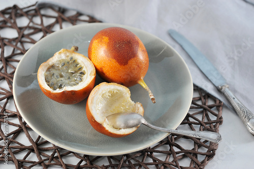 Granadilla is an exotic tropical fruit. Two fruits lie on a plate. One of the fruits is cut in half. In the frame cutlery. Close-up. photo