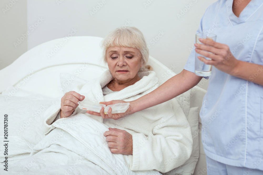 Fototapeta premium Life with drugs. Dismal elder woman lying in bed while consuming drugs