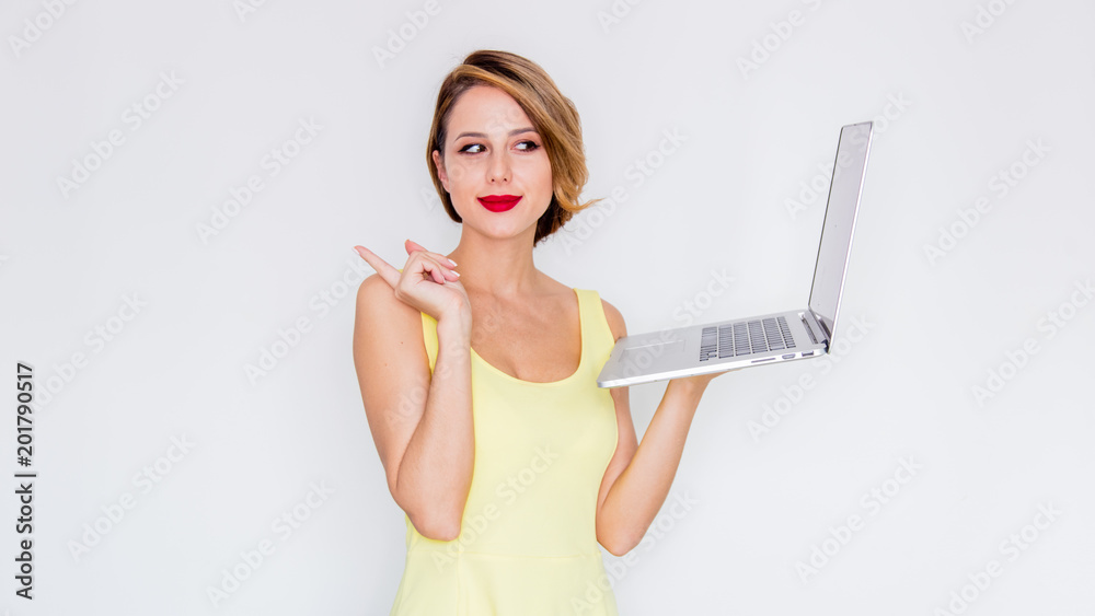 Fototapeta premium Young redhead girl in yellow dress with laptop computer on white background