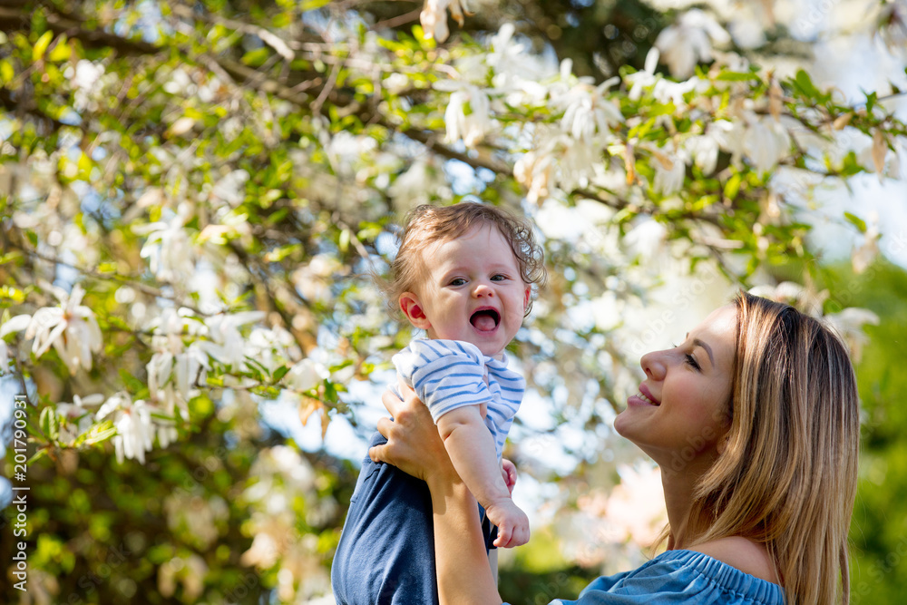 Young redhead mother and child have a leisure in springtime flowering garden in sunny day. Young redhead mother and child have a leisure in springtime flowering garden in sunny day.