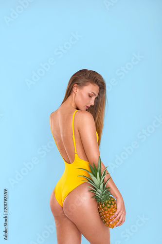 Sexy girl in a yellow swimsuit with a pineapple on a blue background