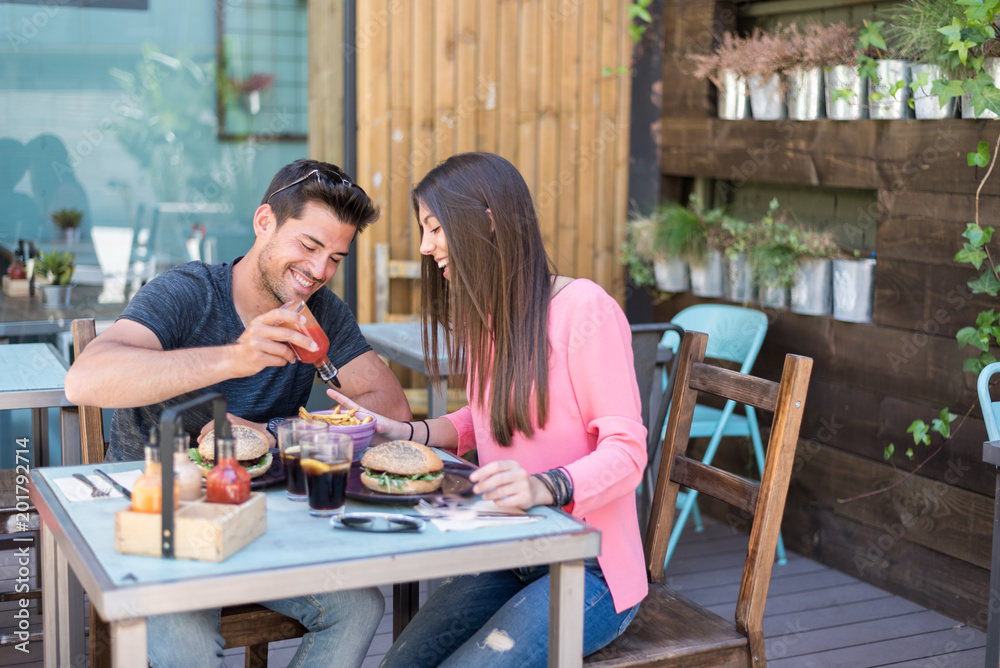 Happy young couple seating in a restaurant terrace eating a burger Happy young couple seating in a restaurant terrace eating a burger