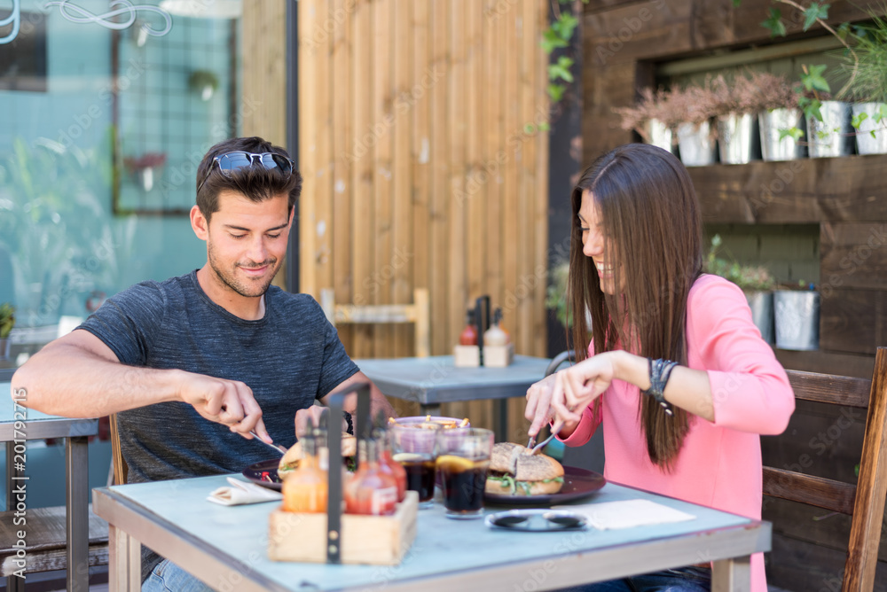 Fototapeta premium Happy young couple seating in a restaurant terrace eating a burger