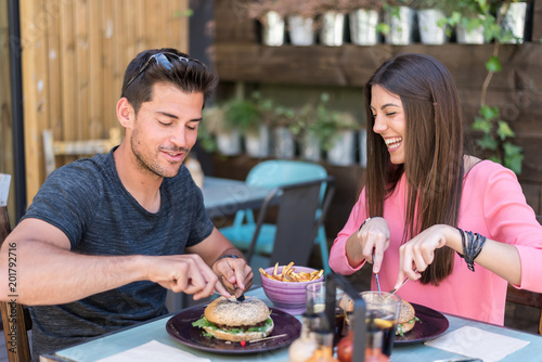 Happy young couple seating in a restaurant terrace eating a burger