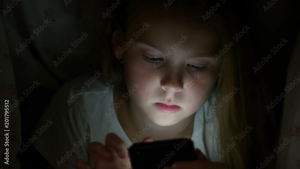 Girl with a smartphone under a blanket at night