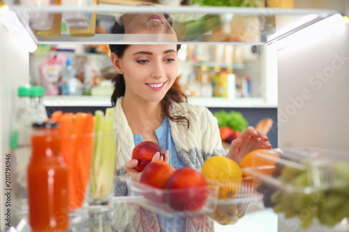 Portrait of female standing near open fridge full of healthy food, vegetables and fruits. Portrait of female