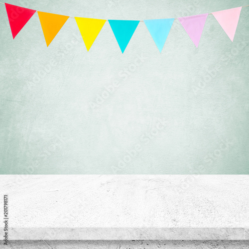 Colorful party flags hanging on green wall and white cement table background, birthday, anniversary, celebrate event, festival greeting card background