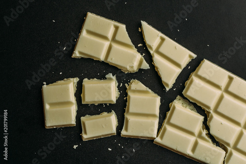 Fotografie Broken white chocolate bar on black, top view