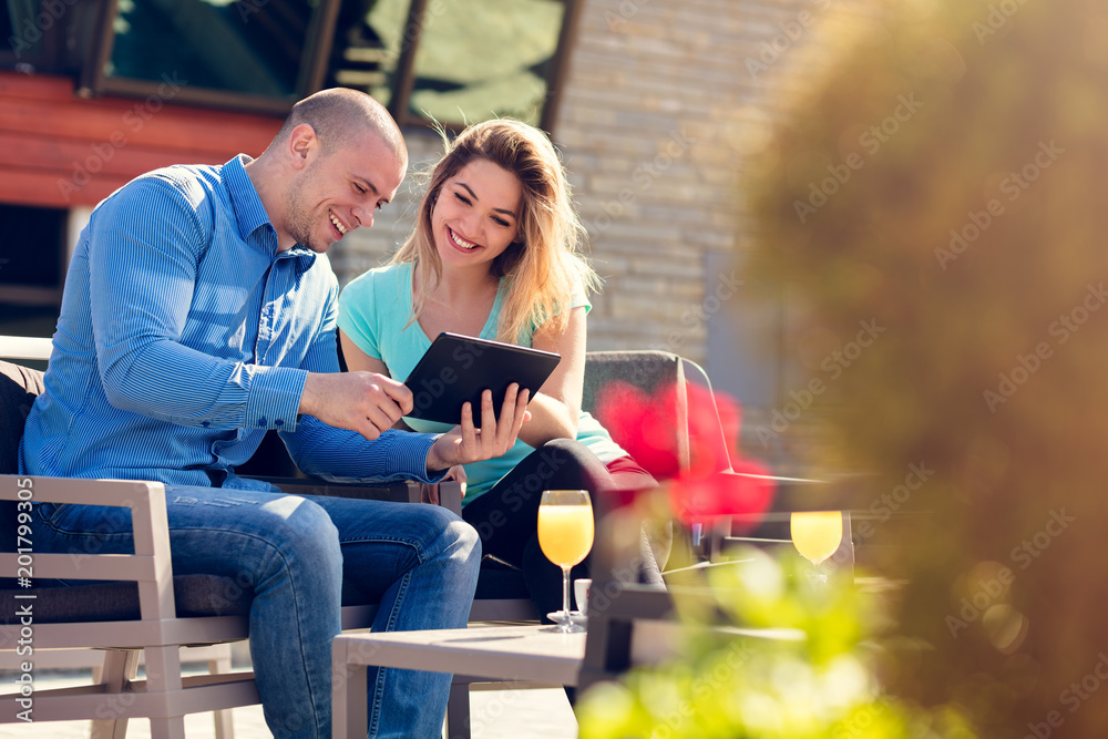 Obraz premium Young couple, woman and man, in street cafe drinking coffee and juice while watching pictures of holidays