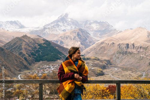 a nice young girl with a warm scarf on her shoulders stands against the background of high mountains, enjoys traveling photo