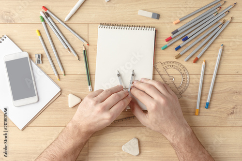 The designer draws a sketch in a notebook on a wooden table. Stationery. View from above. photo