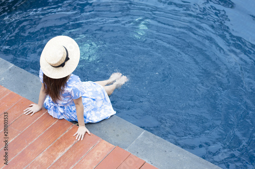 Woman is sitting at the pool side while vacation summer time.