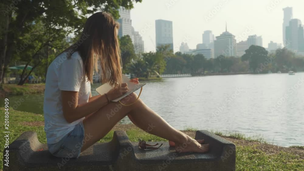 Young woman sitting on the bench in park and writing in diary Young woman sitting on the bench in park and writing in diary