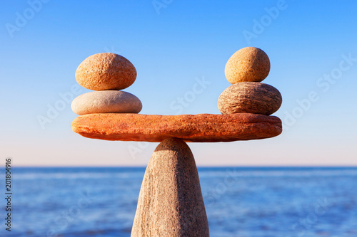 Symbolic scales of the stones, illuminated by the evening sun, against the sea, close-up. Pros and cons concept