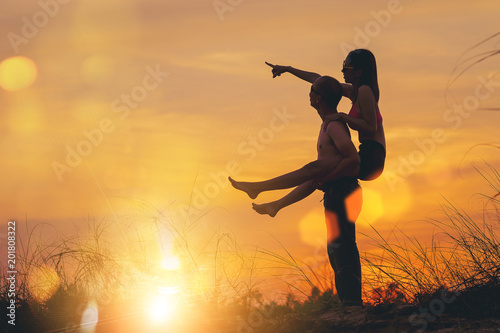 silhouette of happy guy holding his girlfriend in back on sunset background and celebrating freedom in tourism.