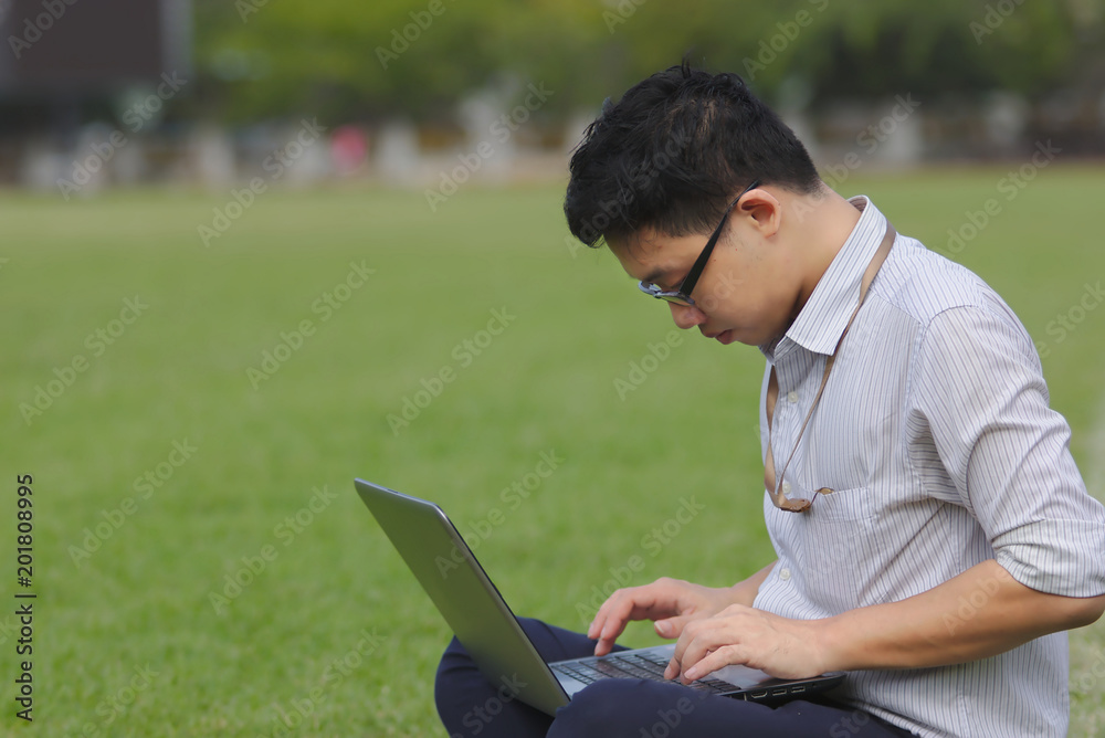 Side view of handsome Asian business man working with laptop on the green grass. Side view of handsome Asian business man working with laptop on the green grass.