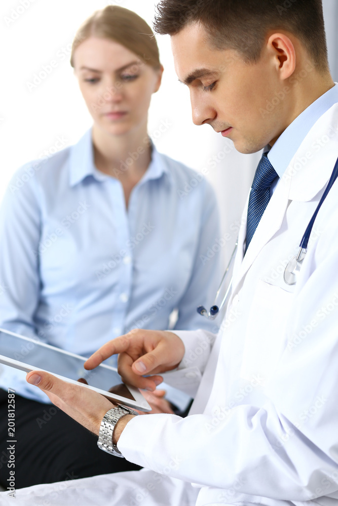 Male doctor using touchpad or tablet pc while consulting female patient in hospital office. Medicine and healthcare concept Male doctor using touchpad or tablet pc while consulting female patient in hospital office. Medicine and healthcare concept