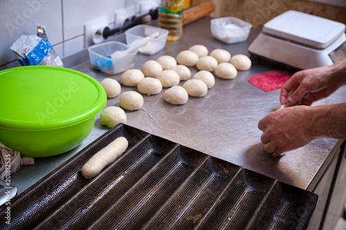 A close-up of a female bakerpulls out the dough for cooking buns for hotdogs on a metal  becary table with a rolling pin