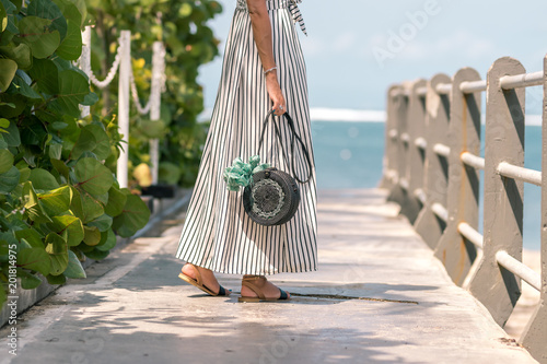 Woman with fashionable stylish rattan bag black color and silk scarf outside. Tropical island of Bali, Indonesia. Rattan handbag and silk scarf. photo