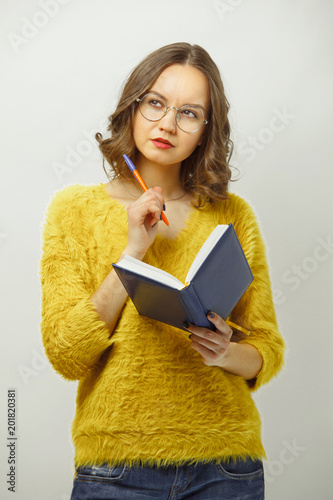 Tablou pe pânză Young woman with notepad and pen in hand, looking up thoughtfully, trying to solve the problem or issue over white isolated background