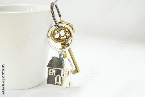 Home keys with house keyring hanging on white coffee cup