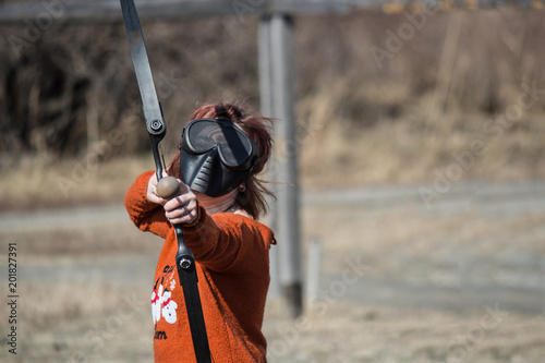 Archer girl in protective mask with bow aim at something in front of him. Archers fight or duel