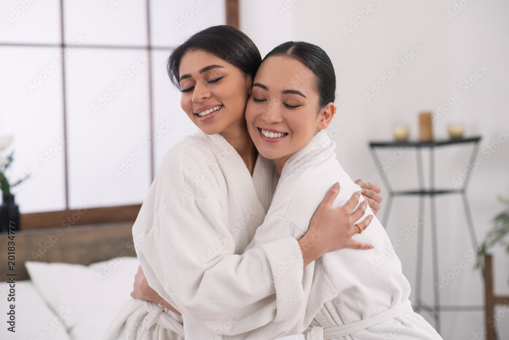 Absolute delight. Delighted joyful women closing their eyed while hugging each other