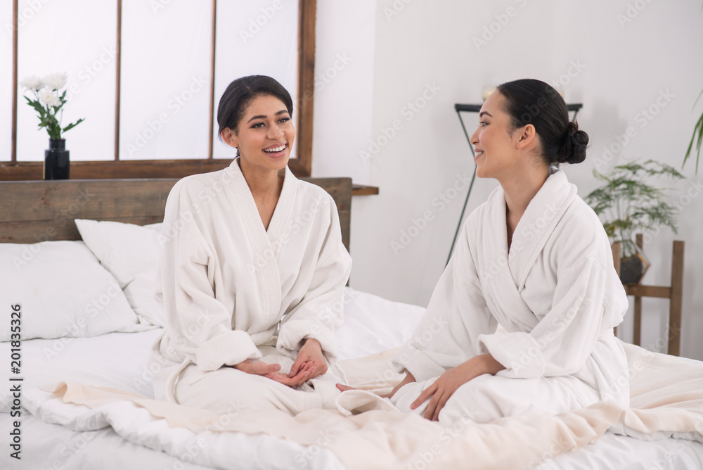 Happy couple. Joyful delighted women sitting in the bed in the spa salon and smiling