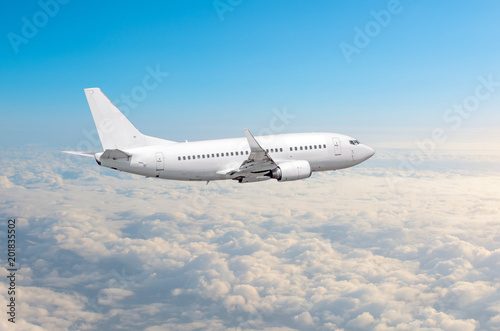 White airplane flies height, flight level high in the sky above the clouds blue sky.