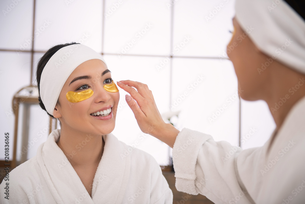 Fresh look. Cheerful young woman looking at her friend while wearing eye patches Fresh look. Cheerful young woman looking at her friend while wearing eye patches