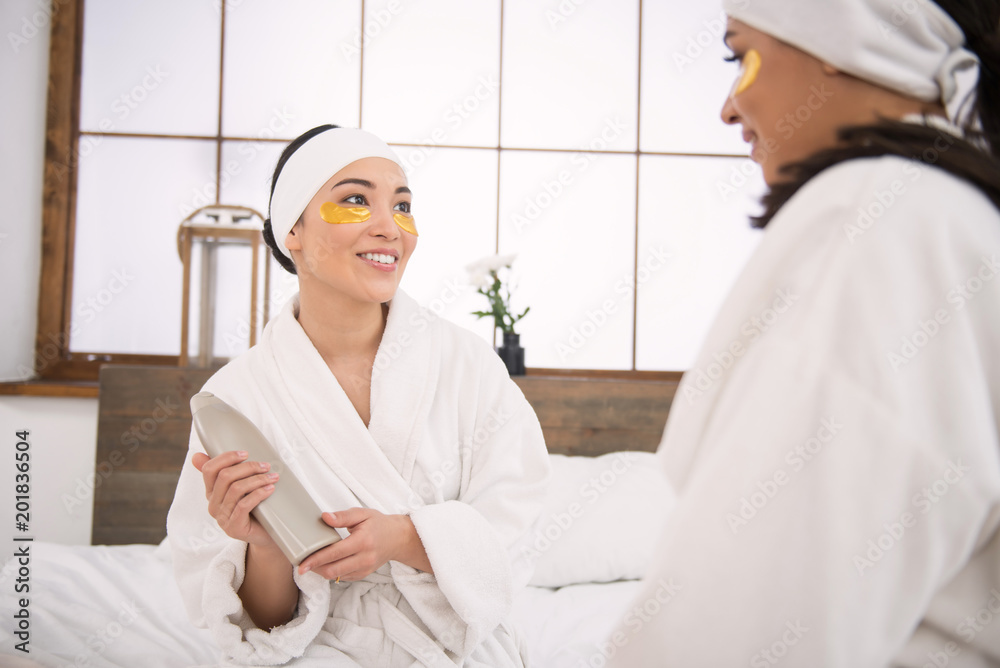 Friends recommendation Delighted happy young woman showing body lotion to her friend while recommending it to her