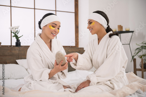 I need it. Positive cheerful woman pointing at the body lotion while talking with her girlfriend in the spa salon