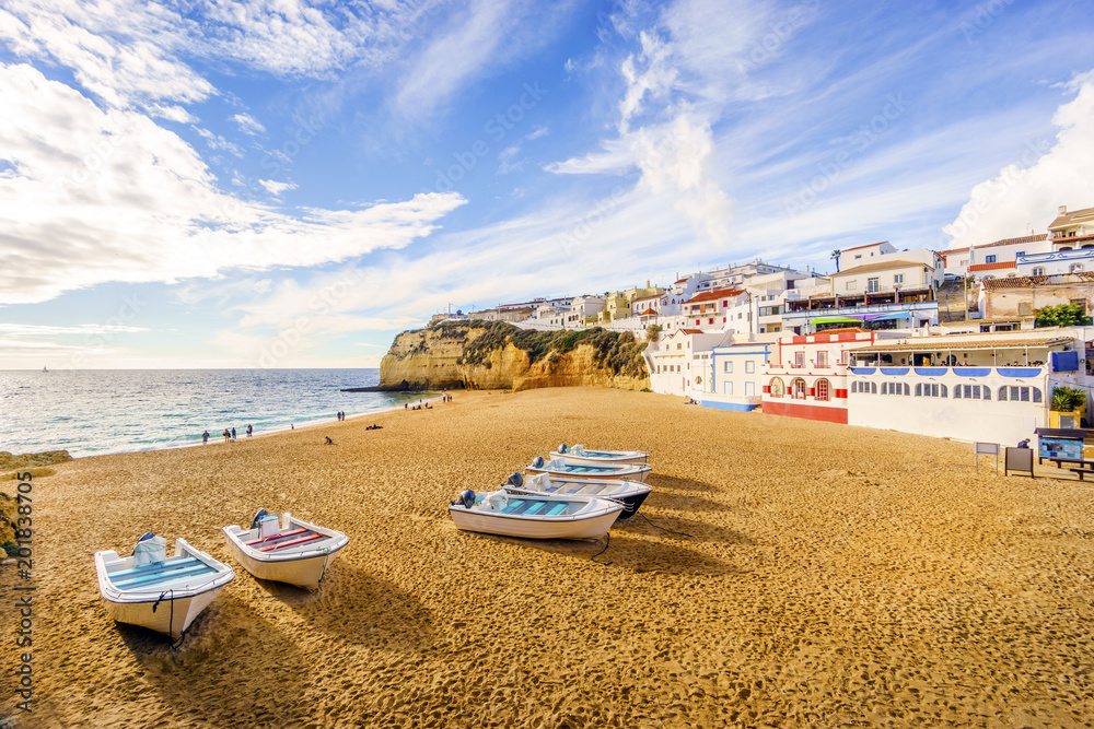 Sandy beach with colorful boats and cliffs and white architecture in Carvoeiro, Algarve, Portugal