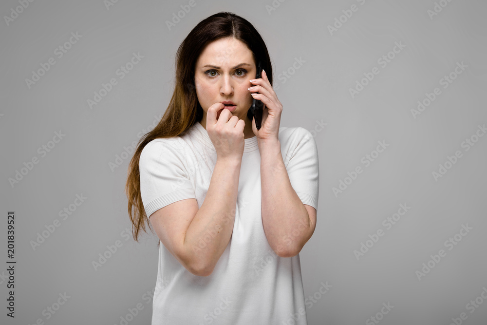 Emotional sad puzzled plus size model standing in studio looking in camera talking on phone with friend Emotional sad puzzled plus size model standing in studio looking in camera talking on phone with friend