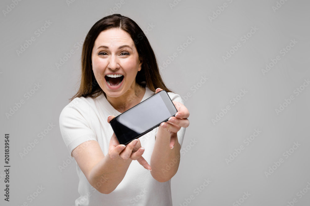 Emotional smiling happy plus size model standing in studio looking in camera offering mobile phone to a client Emotional smiling happy plus size model standing in studio looking in camera offering mobile phone to a client
