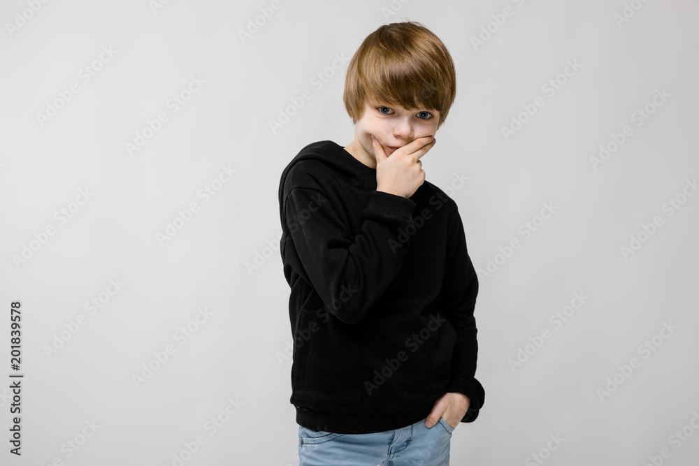 Portrait of adorable confident little boy standing in studio with hand near his face with hand on pocket on grey background Portrait of adorable confident little boy standing in studio with hand near his face with hand on pocket on grey background