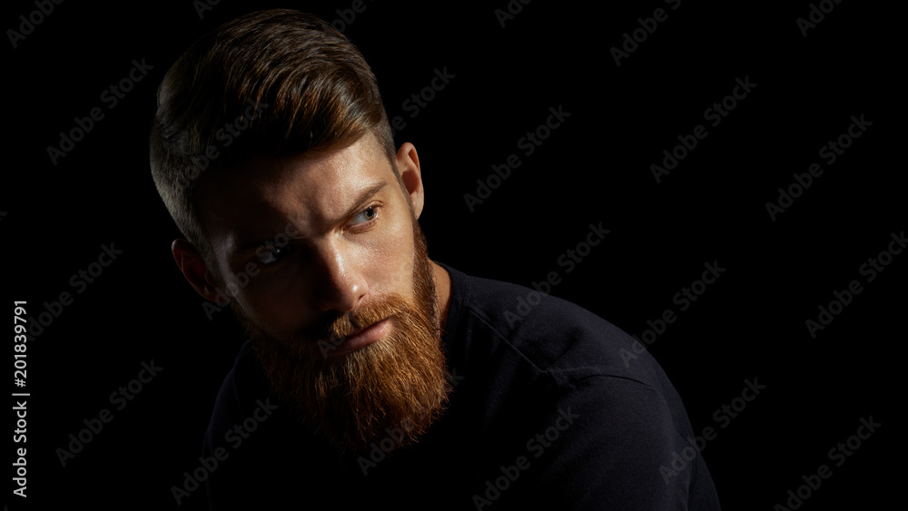 Portrait of young handsome bearded man looking forward Studio shot over black background.