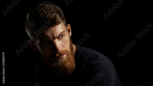 Portrait of young handsome bearded man looking forward Studio shot over black background.
