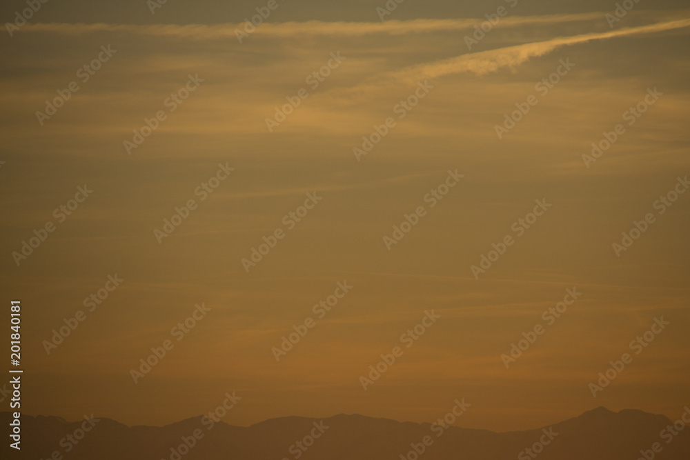 Evening sky after sunset with the alps as horizon line and contrails in the yellow and blue sky