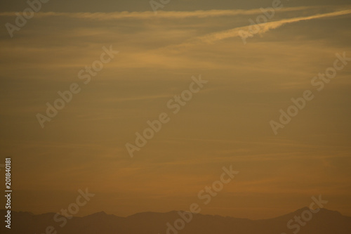 Evening sky after sunset with the alps as horizon line and contrails in the yellow and blue sky