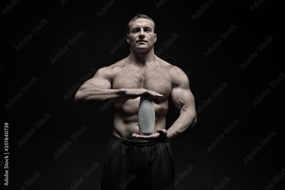 Fototapeta premium Bodycare and hygiene for sportsman. Bodybuilder hold shampoo or gel bottle. Man athlete with fit torso and ab. Spa bath or shower cosmetic after training in gym, vintage