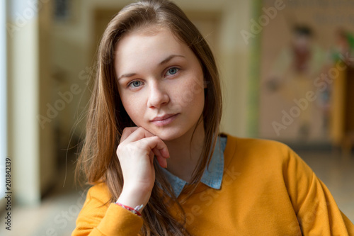 Young happy female college student sitting in the hallway at her school. Education concept.