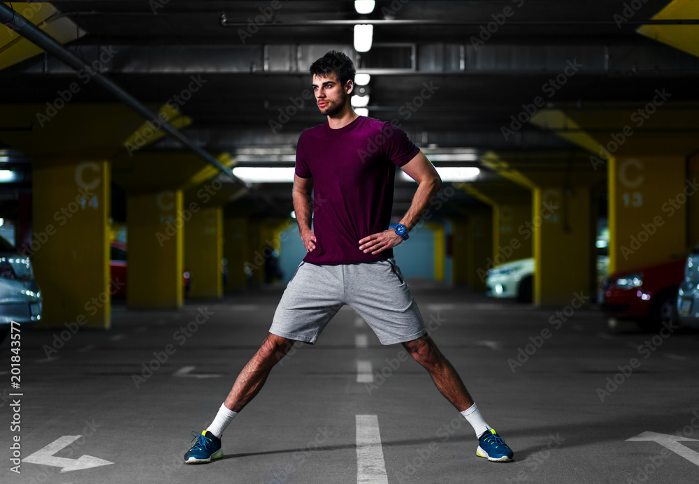 Young male runner stretching his muscles before workout in the underground car parking.