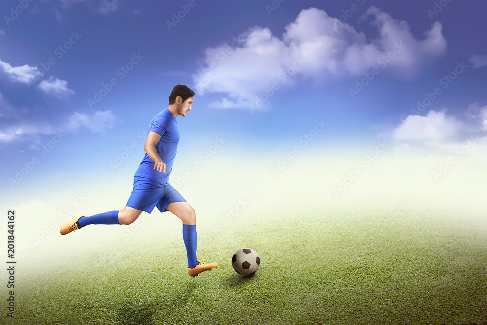 Obraz premium Side view of asian footballer kick the ball