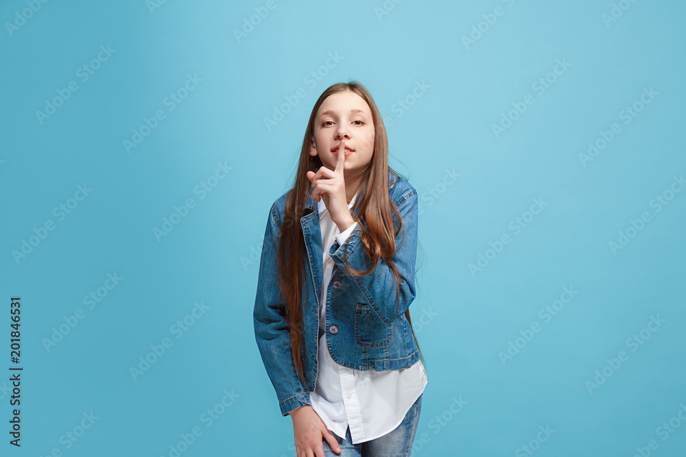 The young teen girl whispering a secret behind her hand over blue background The young teen girl whispering a secret behind her hand over blue background