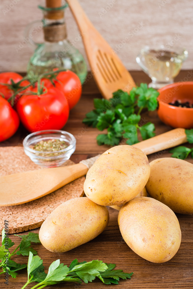 Raw potatoes in the peel, vegetables, greens and spices for cooking a dish on a wooden table Raw potatoes in the peel, vegetables, greens and spices for cooking a dish on a wooden table